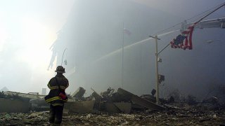 A firefighter walks through rubble of the twin towers of the World Trade Center as a US flag hangs from a traffic light post 11 September, 2001, in New York. Two planes controlled by hijackers crashed into the buildings, destroying both.