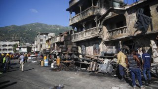 Firefighters stand next to what remains of a truck that was carrying gasoline after it overturned and exploded in Cap-Hatien, Haiti,