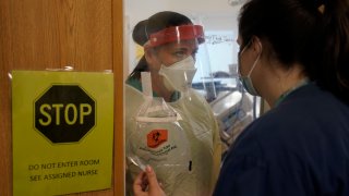 Clinical Nurse Supervisor Melinda Chapin, of Holderness, N.H., left, communicates through glass from inside a COVID-19 isolation room with registered nurse Rachel Chamberlin, of Cornish, N.H., right, at Dartmouth-Hitchcock Medical Center, in Lebanon, N.H., Monday, Jan. 3, 2022. Doctors and nurses, once lauded for their service, complain about burnout and a sense their neighbors are no longer treating the pandemic as a health emergency — despite day after day of record COVID-19 cases in the state.