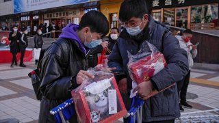 People inspect their purchases outside a store selling 2022 Winter Olympics memorabilia in Beijing, Monday, Feb. 7, 2022. The race is on to snap up scarce 2022 Winter Olympics souvenirs. Dolls of mascot Bing Dwen Dwen, a panda in a winter coat, sold out after buyers waited in line overnight in freezing weather.