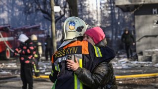 A fireman embraces a woman outside a damaged apartment building in Kyiv on March 15, 2022, after strikes on residential areas killed at least two people, Ukraine emergency services said as Russian troops intensified their attacks on the Ukrainian capital.