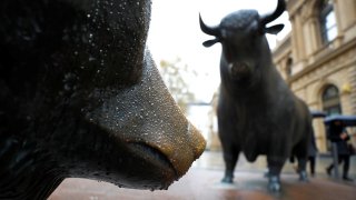 People with umbrellas pass by bull and bear outside Frankfurt’s stock exchange during heavy rain in Frankfurt, Germany.