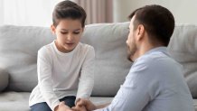 Worried loving young single father holding hand talking comforting upset little kid son sharing helping with problem, caring dad foster parent give support apologizing supporting listening child boy