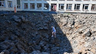 A woman stands in a crater caused by missile strikes which struck the yard of a school in a residential area of Kharkiv on June 27,2022, amid the Russian invasion of Ukraine.