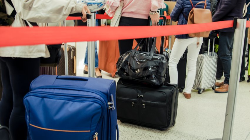 People standing in a large queue at the airport with their luggage, the queue is long and people are starting to get bored.