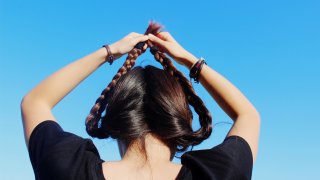 Woman Holding Braided Hair Up Against Clear Sky