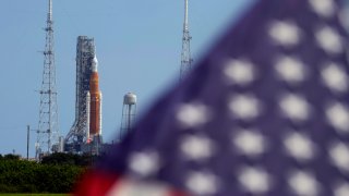 FILE - An American flag flies in the breeze as NASA's new moon rocket sits on Launch Pad 39-B