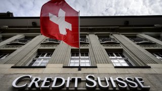 A Swiss flag flies over a sign of Credit Suisse in Bern, Switzerland