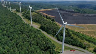 In an aerial view, turbines from the Roth Rock wind farm spin on the spine of Backbone Mountain next to the Mettiki Coal processing plant on August 23, 2022 in Oakland, Maryland.