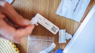 A woman squeezing the sample liquid on a test strip while carrying out a Covid-19 rapid self test at home.