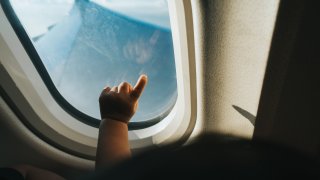 Cropped hand of a toddler pointing at an airplane window against blue sky
