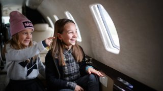 Two sisters sitting inside private jet airplane and looking outside the window.