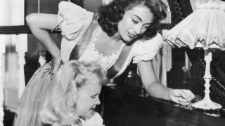 Joan Crawford supervises her adoptive daughter Christina's piano practice.