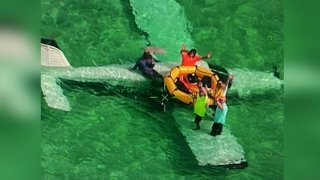 Five people sitting on the wings of a plane crashed in the ocean wave at a rescuer in the sky.