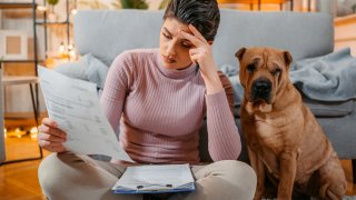 Worried young woman checking her finances while sitting on the floor at home, with her cute shar-pei dog.