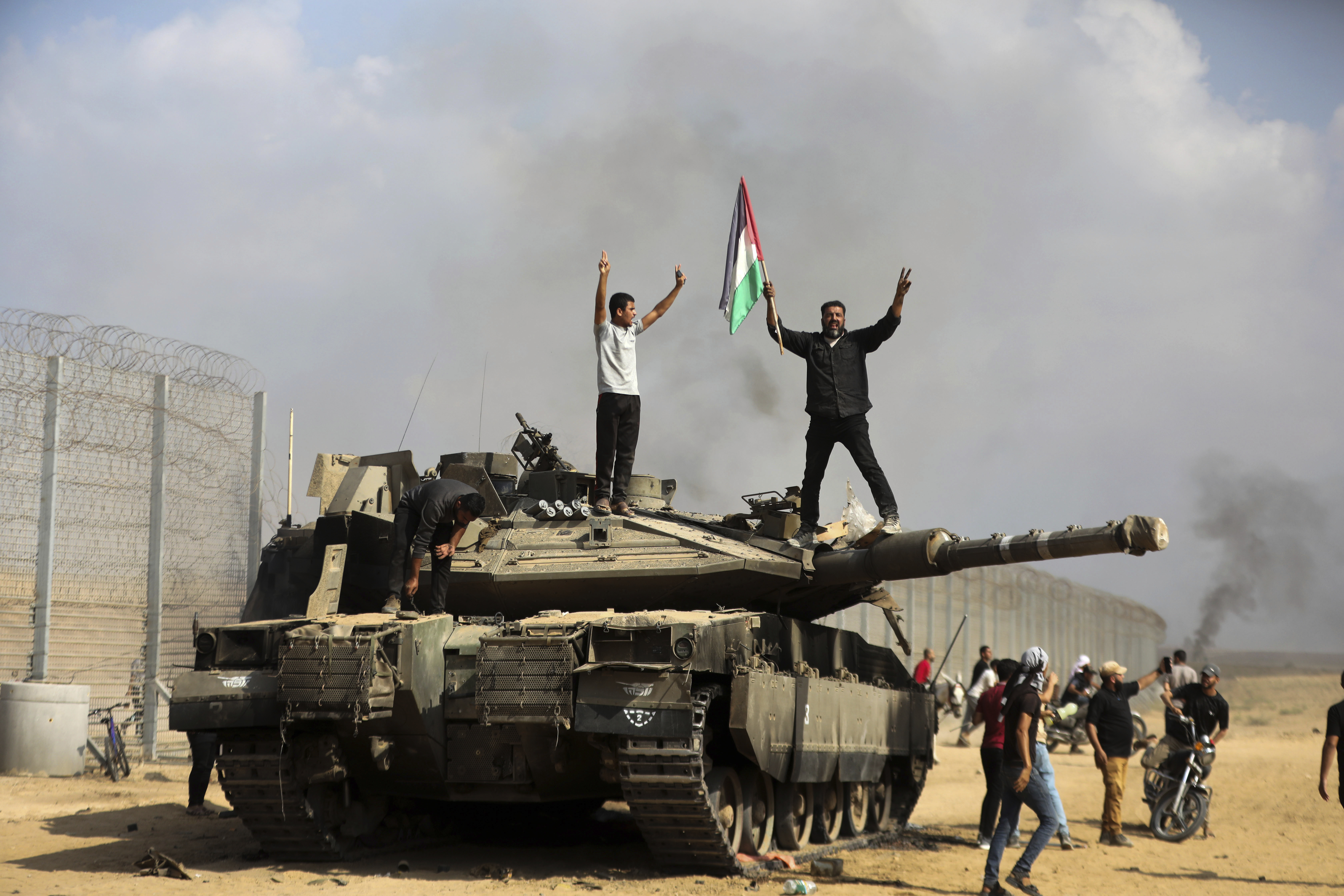 Palestinians wave their national flag and celebrate by a destroyed Israeli tank at the Gaza Strip fence east of Khan Younis southern Saturday, Oct. 7, 2023.