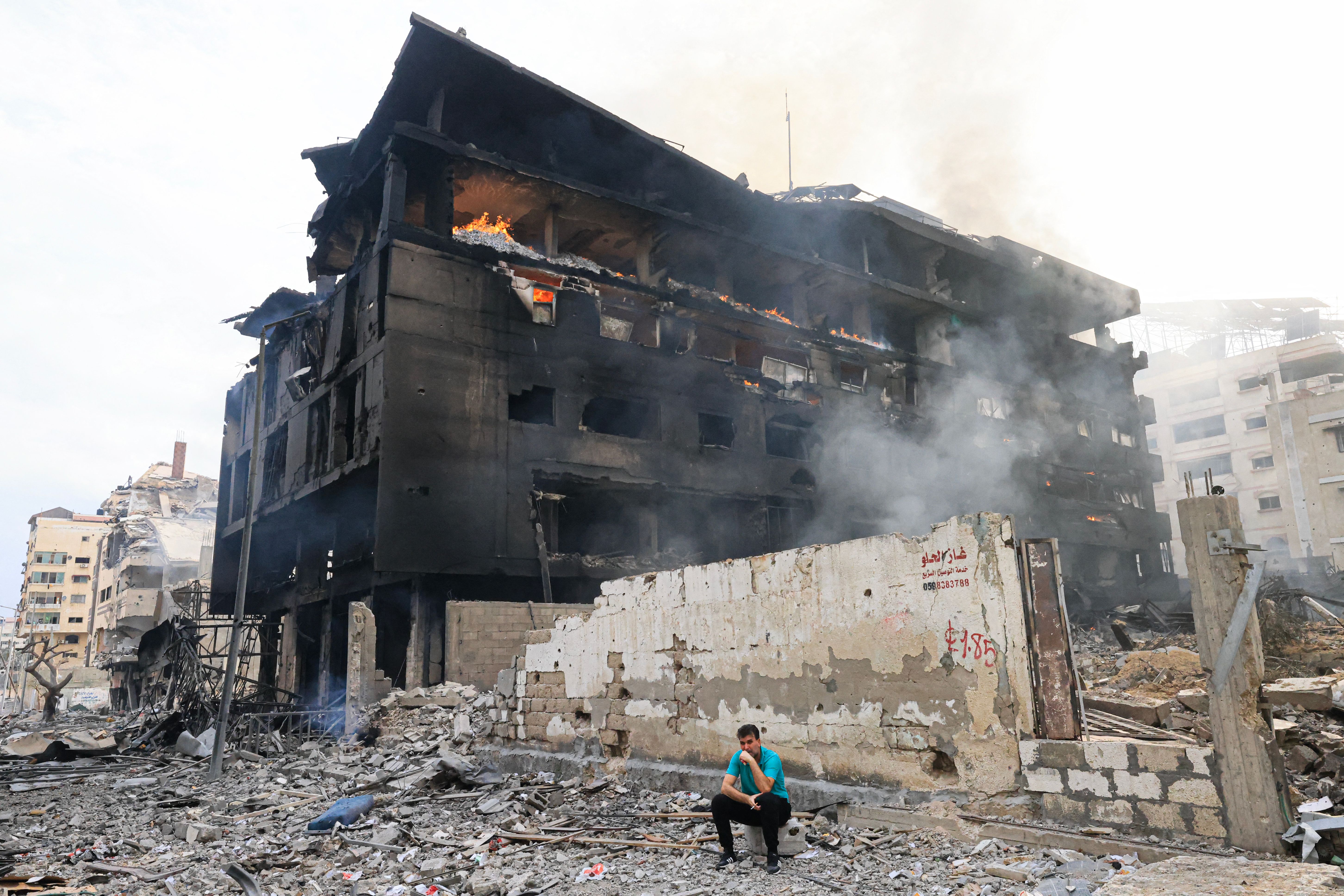 A Palestinian man sits in front of a charred building as a fire rages through its interior, following Israeli airstrikes in Gaza City&#8217;s al-Rimal district on Oct. 10, 2023.