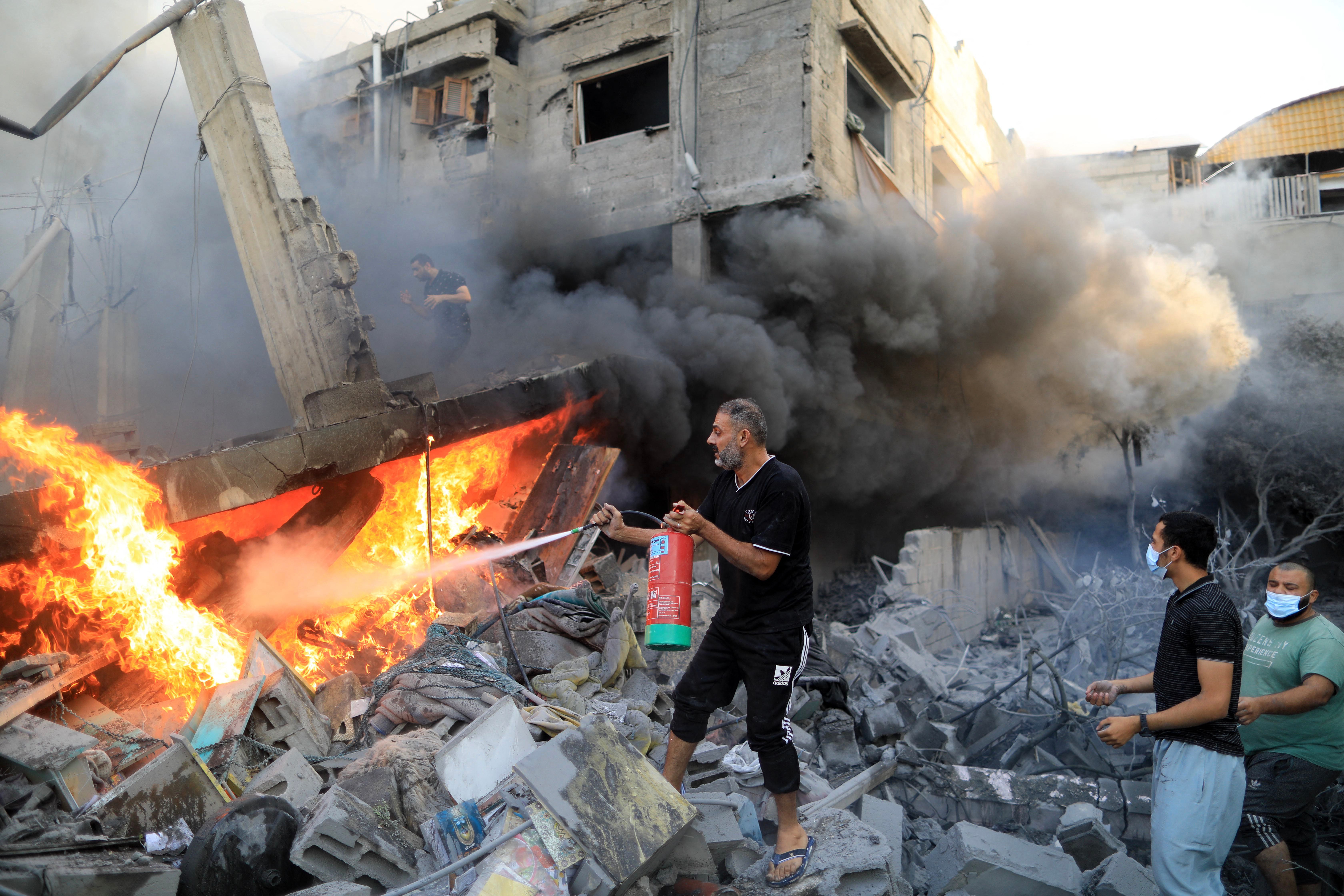 A Palestinian man uses a fire extinguisher to douse a fire following an Israeli strike, in Khan Yunis in the southern Gaza Strip on Oct. 14, 2023.