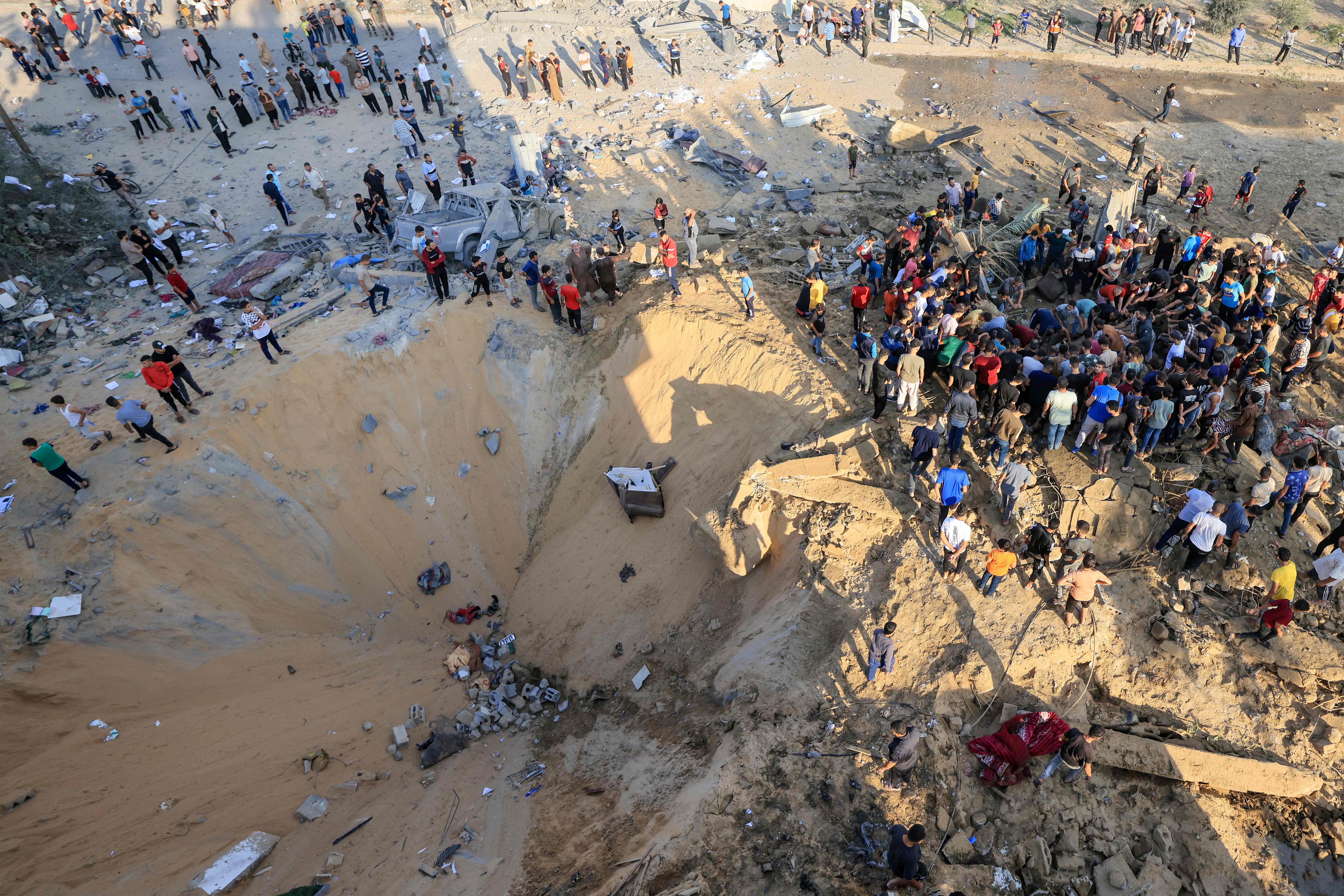 Palestinians stand next to a crater caused by an explosion from an Israeli airstrike in Khan Yunis in the southern of Gaza Strip, on Oct. 16, 2023.