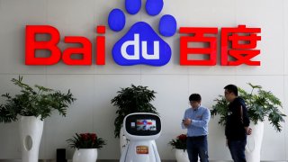 Men interact with a Baidu AI robot near the company logo at its headquarters in Beijing, China April 23, 2021.