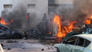 People try to extinguish fire on cars following a rocket attack from the Gaza Strip in Ashkelon, southern Israel, on October 7, 2023.