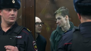 Artyom Kamardin, left, and Yegor Shtovba, right, stand behind a glass in a cage