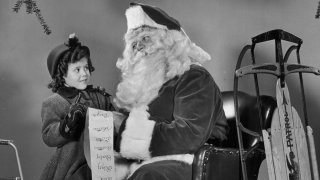 A little girl, wearing a winter coat, gives Santa Claus her wish list