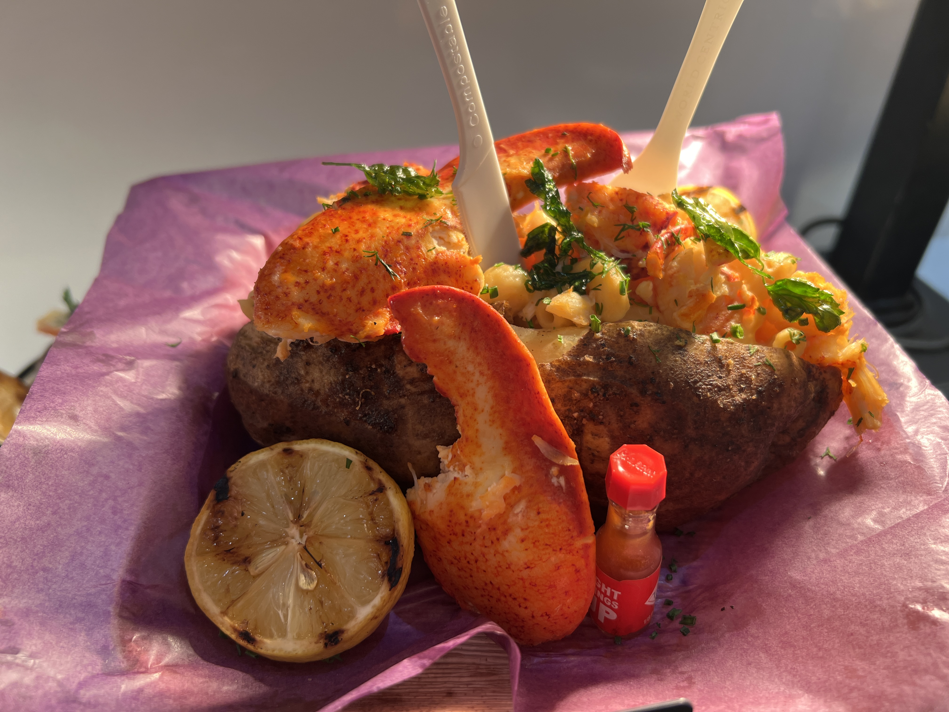 Colossal baked potato stuffed with creamy mac and cheese, and topped with King crab legs, Maine lobster, grilled lemon, and mini Tabasco bottles.  Available at Allegiant Stadium for Super Bowl 58.