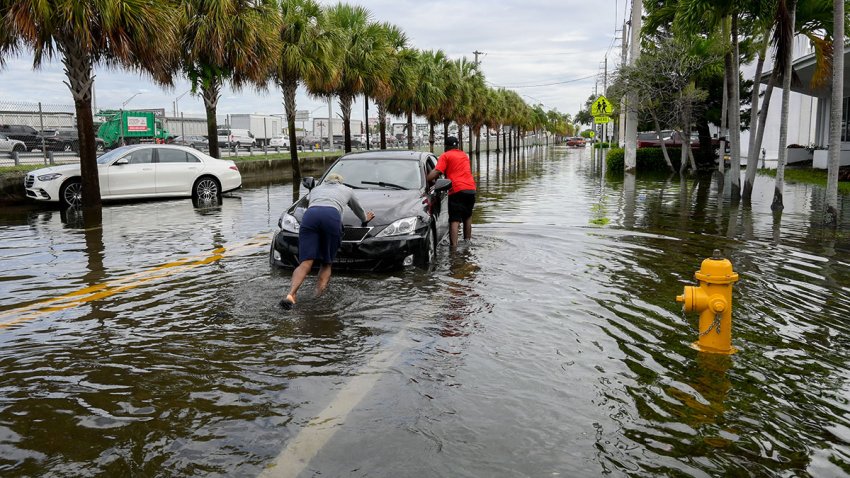 MIAMI, FLORIDA – JUNE 13: 2 people push a car out of one of the flooded streets, after 24 hours of continuous rain in South Florida on June 13, 2024 (Photo by Jesus Olarte/Anadolu via Getty Images)