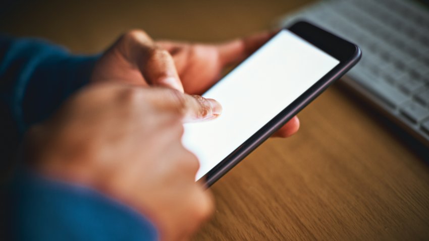 Male hands tap mobile phone screen, keyboard in background