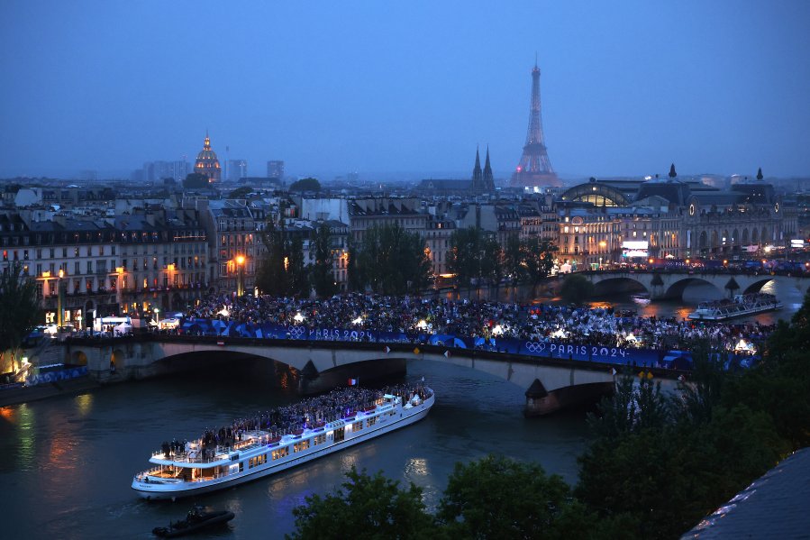 Spectators look on as athletes from Team France pass by on a boat on the River Seine