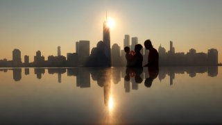 The sun rises behind the skyline of lower Manhattan and One World Trade Center as people walk along the Hudson River on September 14, 2024, in Jersey City, New Jersey. 