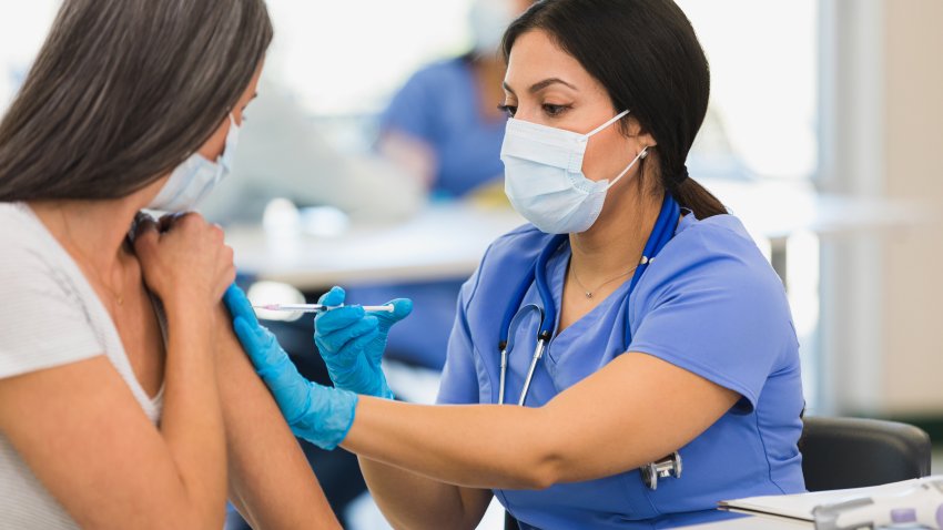 A close up photo of a mid adult female nurse giving a vaccine to an unrecognizable mid adult woman at a vaccination center.