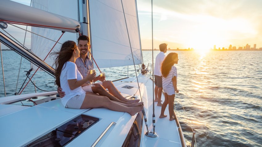 Smiling Latin American parents enjoying fun family vacation with children on luxury yacht sailing towards cityscape at sunrise