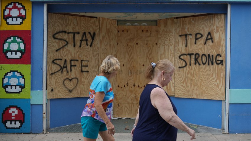 People walk past boarded up storefronts in Tampa ahead of Hurricane Milton’s expected landfall in the middle of this week on October 8, 2024 in Florida. Hurricane Milton exploded in strength October 7 to become a potentially catastrophic Category 5 storm bound for Florida, threatening the US state with a second ferocious hurricane in as many weeks. (Photo by Bryan R. SMITH / AFP) (Photo by BRYAN R. SMITH/AFP via Getty Images)