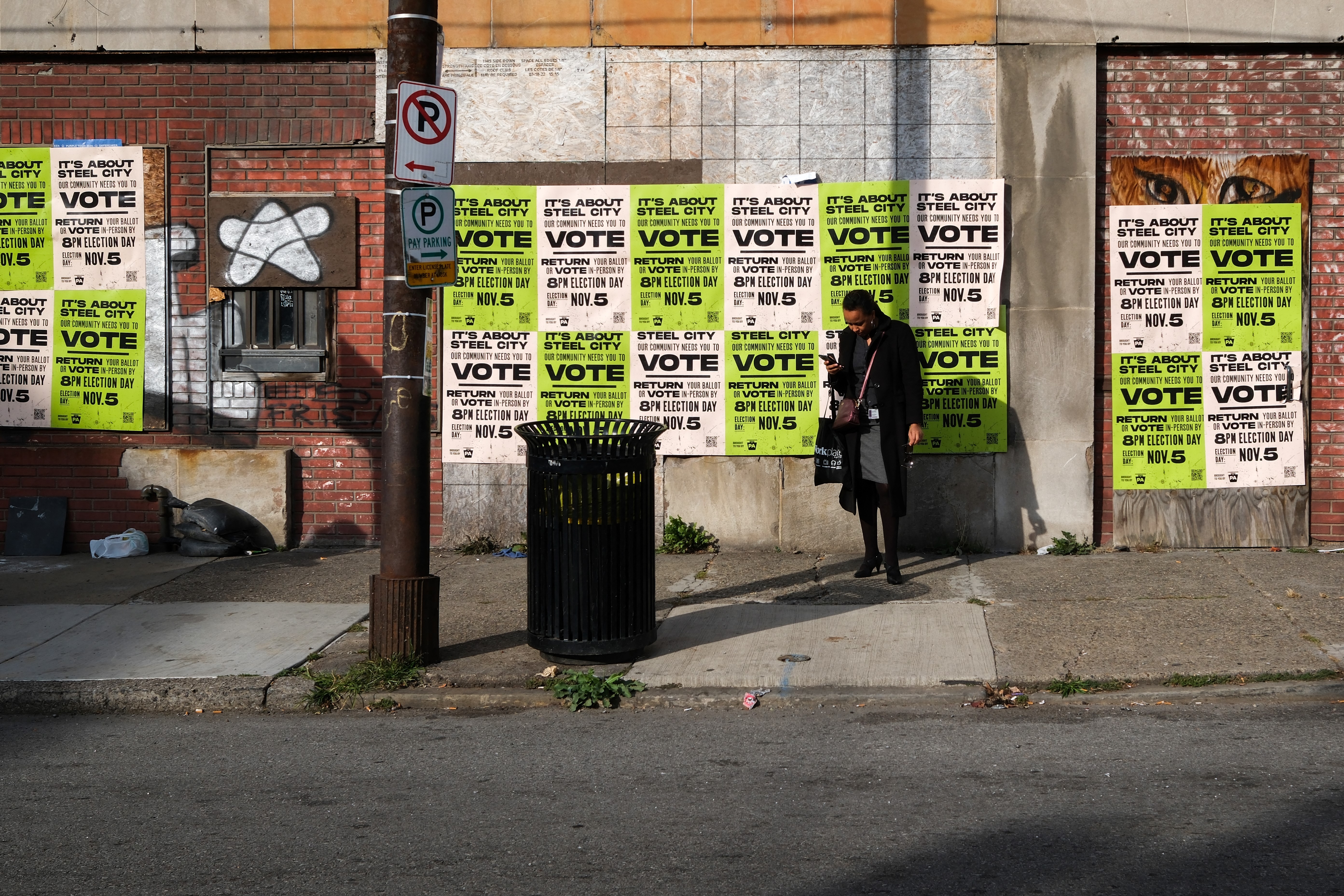 A woman waits for the bus before a wall covered with posters encouraging people to vote in Pittsburgh, Pennsylvania, on November 4, 2024, one day before the US presidential election.