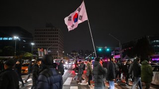 A man holds the South Korea flag outside the National Assembly in Seoul on December 4, 2024, after President Yoon Suk Yeol declared emergency martial law. South Korea’s President Yoon Suk Yeol on December 3 declared emergency martial law, saying the step was necessary to protect the country from “communist forces” amid parliamentary wrangling over a budget bill.