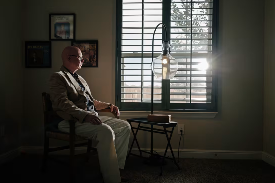 Tim Leggett sits in front of a window in a darkened room and looks out the window.