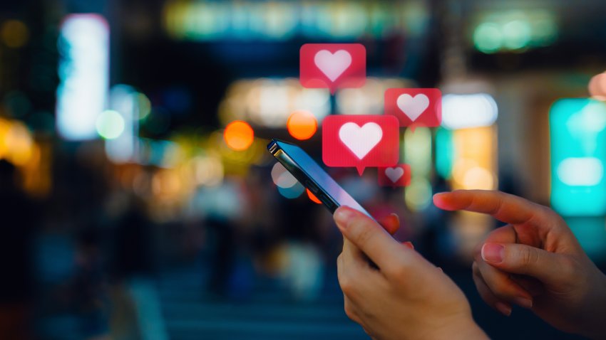 Young woman connecting with social media network on smartphone. Receiving notifications, viewing posts, giving likes on social media posts. With heart shape emoji speech bubble message on device screen. People engaging in networking with technology