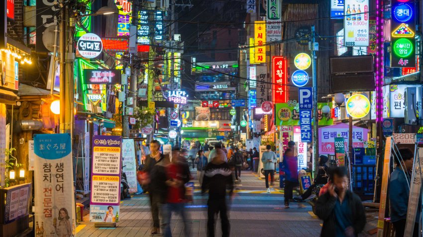 People walking through the neon lit night streets of Sinchon in the heart of Seoul, South Korea’s vibrant capital city.
