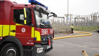 A police officer and firefighters at the North Hyde electrical substation which caught fire. More than 1,300 flights to and from Heathrow Airport will be disrupted on Friday due to the closure of the airport following the fire. Picture date: Friday March 21, 2025.
