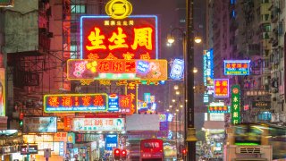 Vibrant neon signs and bright street lights glowing above the busy night traffic of taxis, double decker buses and pedestrians along Nathan Road in the crowded Tsim Sha Tsui district of Kowloon, Hong Kong, China.