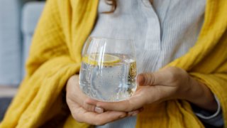 Hands of woman holding sparkling water with lemon slice in glass