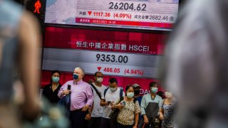 People standing in front of an electronic display showing the Hang Seng Index in the Central district of Hong Kong on July 26, 2021, after stocks plunged as tuition firms were hammered by China’s decision to reform the private education sector by preventing them from making profits.
