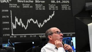 A stock market trader watches his monitors on the trading floor of the Frankfurt Stock Exchange in front of the display board showing the Dax curve.