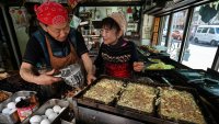 Shop owners of a 70-year-old “takoyaki”, or octopus balls, restaurant chat while cooking along a street in the Taito Ward area of Tokyo on February 21, 2025.