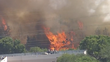 People watch a grass fire burn in southwest Miami-Dade from the roof of a nearby building on May 14, 2025.