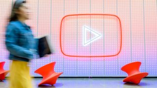 People walk by a YouTube logo as Google celebrates the 20th anniversary of the first video uploaded to YouTube, at the company’s corporate headquarters in San Bruno, California, on April 23, 2025.