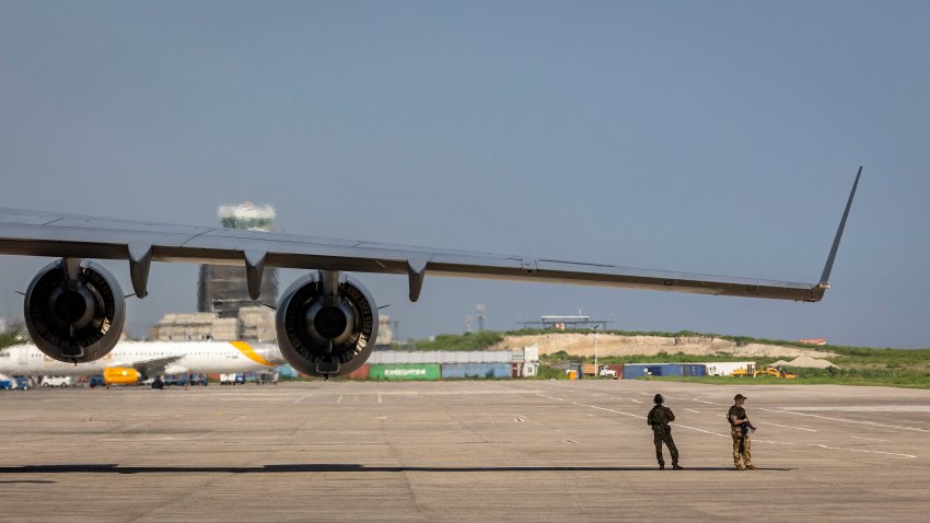 Two United States servicemen take refuge from the searing sun under the wing of a U.S. Air Force C-17 on the tarmac at Toussaint Louverture International Airport in Port-au-Prince, Haiti, May 15, 2024. The plane was carrying supplies for the camp being built for Kenyan police officers who will lead a Multinational Security Support mission into Haiti. (Jose A. Iglesias/Miami Herald/Tribune News Service via Getty Images)