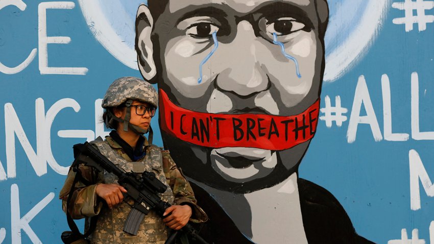 FILE — In this June 4, 2020 file photo a member of the California National Guard stands in front of a mural depicting George Floyd in Los Angeles.